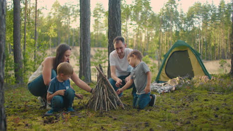 Family-sits-around-a-campfire-on-a-summer-evening.-Children-with-their-parents-are-resting-in-the-woods.-Weekend-in-nature-in-good-company.-Family-frying-sausages-over-a-fire-in-the-woods.